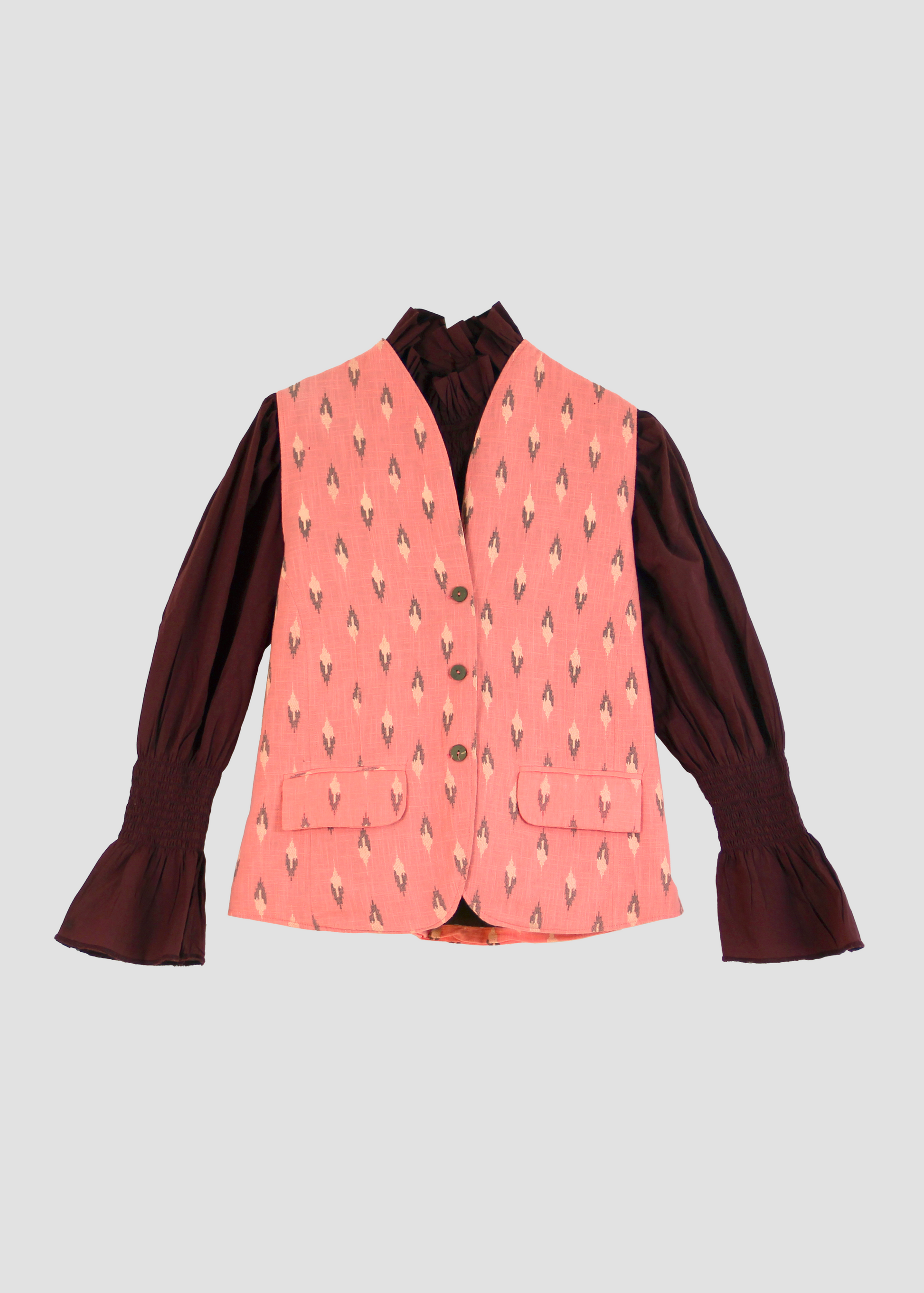 Gilet Madeleine in lino rosa di IGI Ama, smanicato rosa salmone con motivo a rombi, metà rosa chiaro e metà marrone. Realizzato in lino con pattern ikat e interno in velluto a coste. Stile elegante e raffinato, prodotto eticamente in India. Lavabile in lavatrice a 30°C, stirare a bassa temperatura.