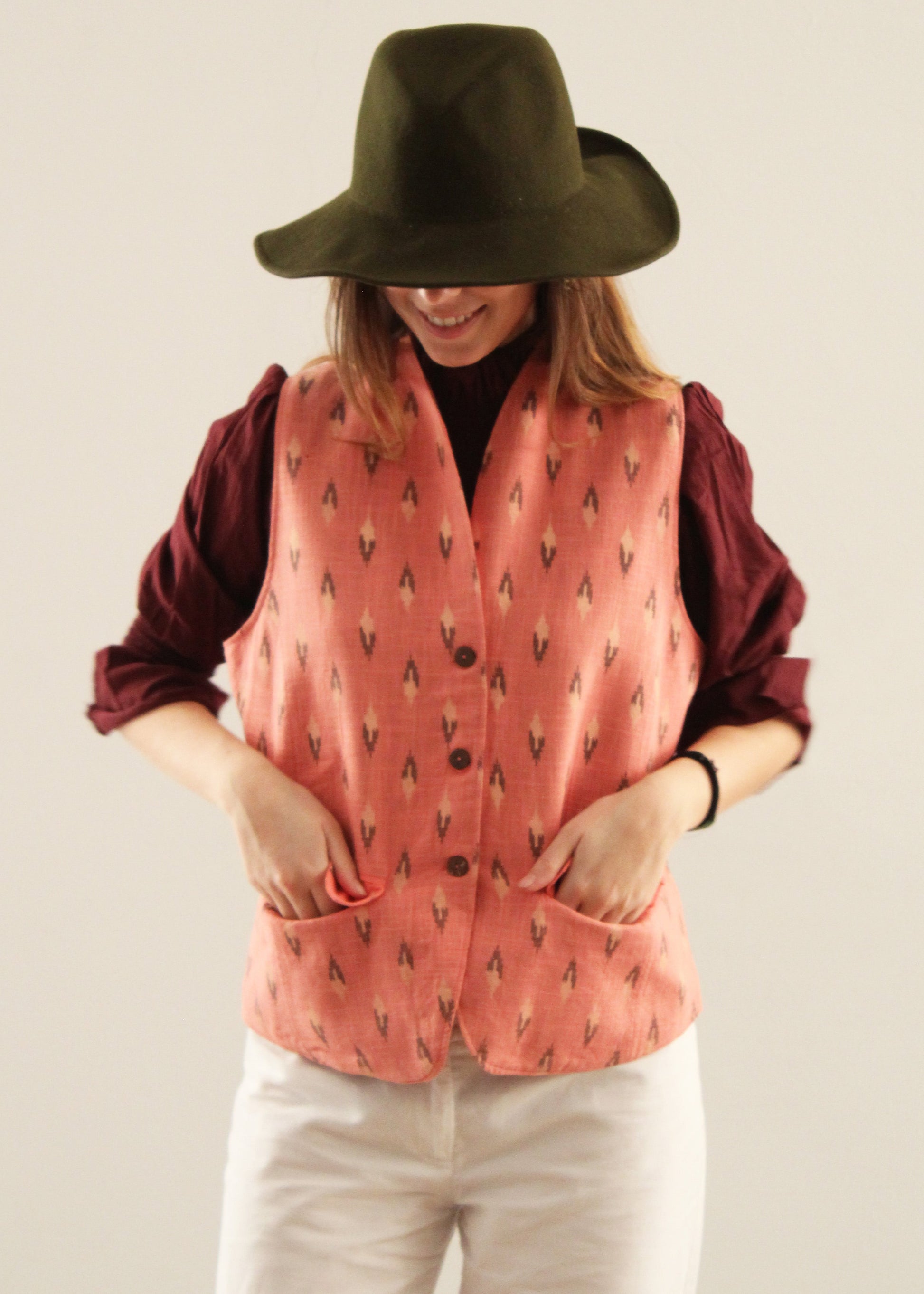 Gilet Madeleine in lino rosa di IGI Ama, smanicato rosa salmone con motivo a rombi, metà rosa chiaro e metà marrone. Realizzato in lino con pattern ikat e interno in velluto a coste. Stile elegante e raffinato, prodotto eticamente in India. Lavabile in lavatrice a 30°C, stirare a bassa temperatura.