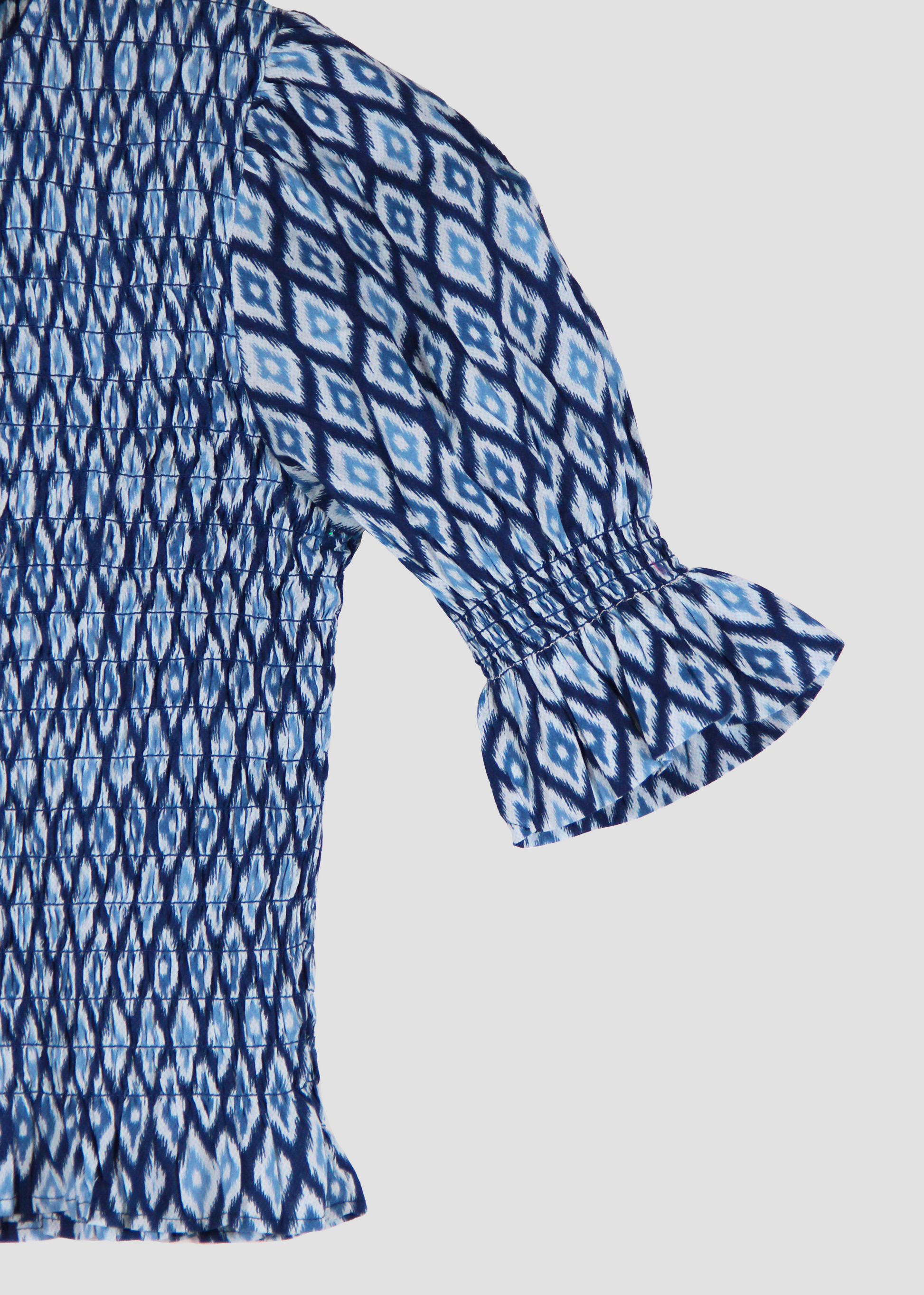 Holi Blouse – Camicetta ikat a maniche corte, realizzata in 100% cotone con maniche a sbuffo e arricciature elastiche su busto e maniche. Vestibilità elasticizzata e confortevole, adatta a tutte le corporature. Taglia unica. Prodotta eticamente in India. Cura delicata: lavare a 30°C, stirare a bassa temperatura.