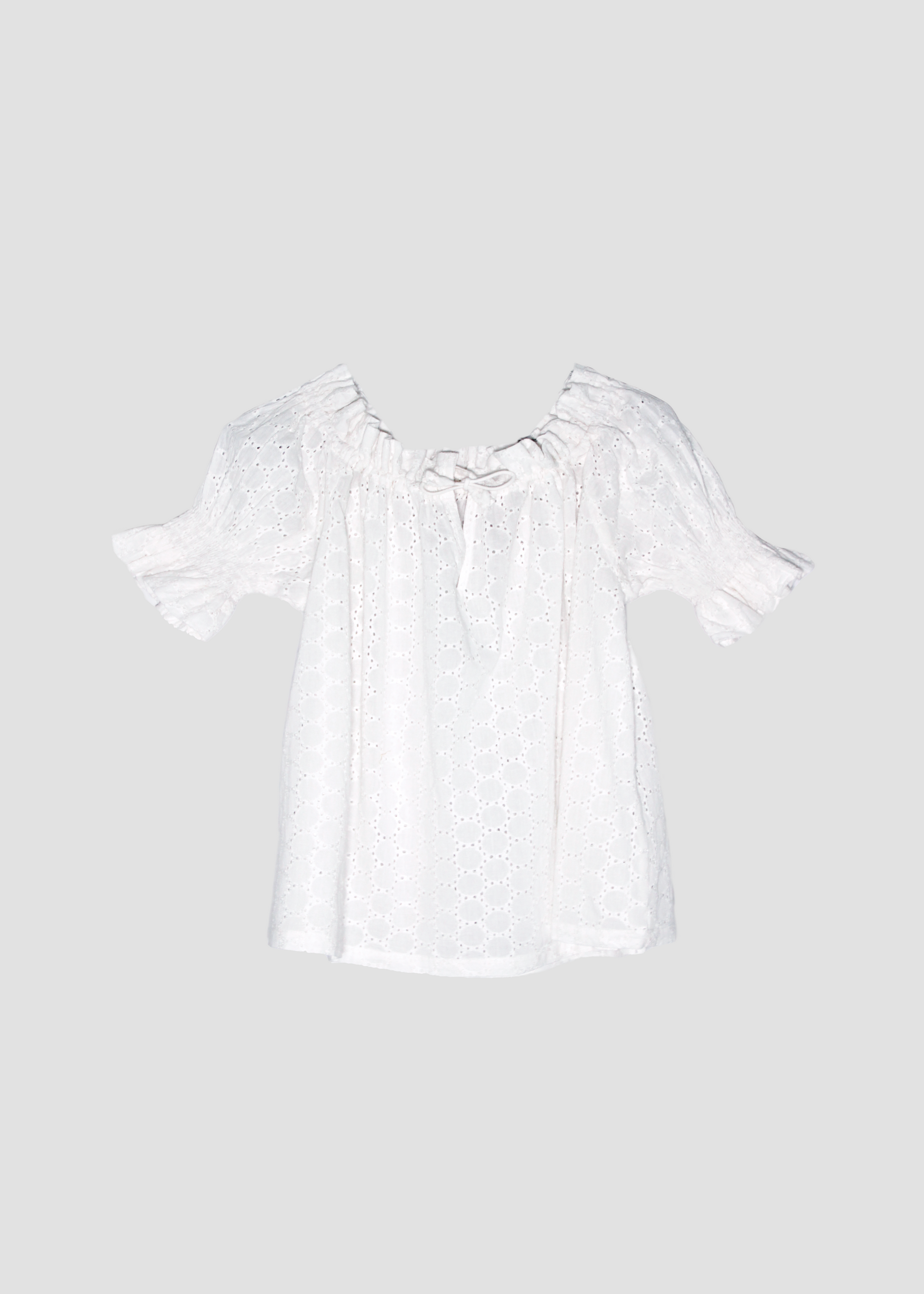 Blusa arricciata da donna in cotone bianco con trama sangallo, modello Pimpa shirt di IGI AMA, 100% cotone, con laccetto sullo scollo e maniche elasticizzate a sbuffo, tessuto elastico che si adatta a tutte le corporature, prodotta in India, ideale per look estivi e casual.