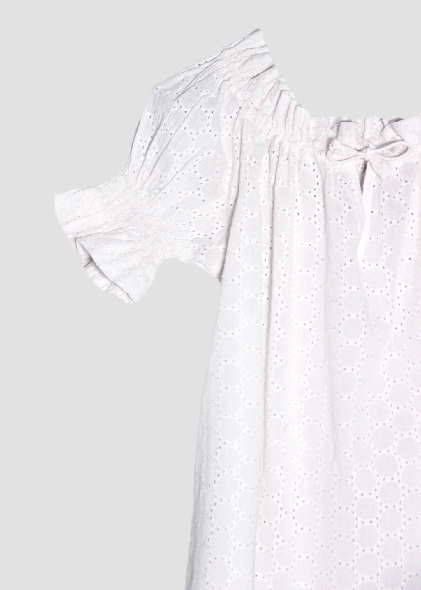 Blusa arricciata da donna in cotone bianco con trama sangallo, modello Pimpa shirt di IGI AMA, 100% cotone, con laccetto sullo scollo e maniche elasticizzate a sbuffo, tessuto elastico che si adatta a tutte le corporature, prodotta in India, ideale per look estivi e casual.