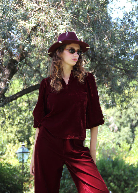 Set autunno/inverno da donna IGI AMA in velluto bordeaux, composto da blusa Bohémien con scollo con chiusura a bottoni in tessuto e maniche lunghe elasticizzate sul polso, e pantaloni in velluto da portare a vita alta o bassa con vestibilità comoda adatta a tutte le corporature, 100% velluto, taglia unica (veste una M), perfetto per outfit vintage chic, look boho radical e abbinamenti eleganti per la stagione fredda.