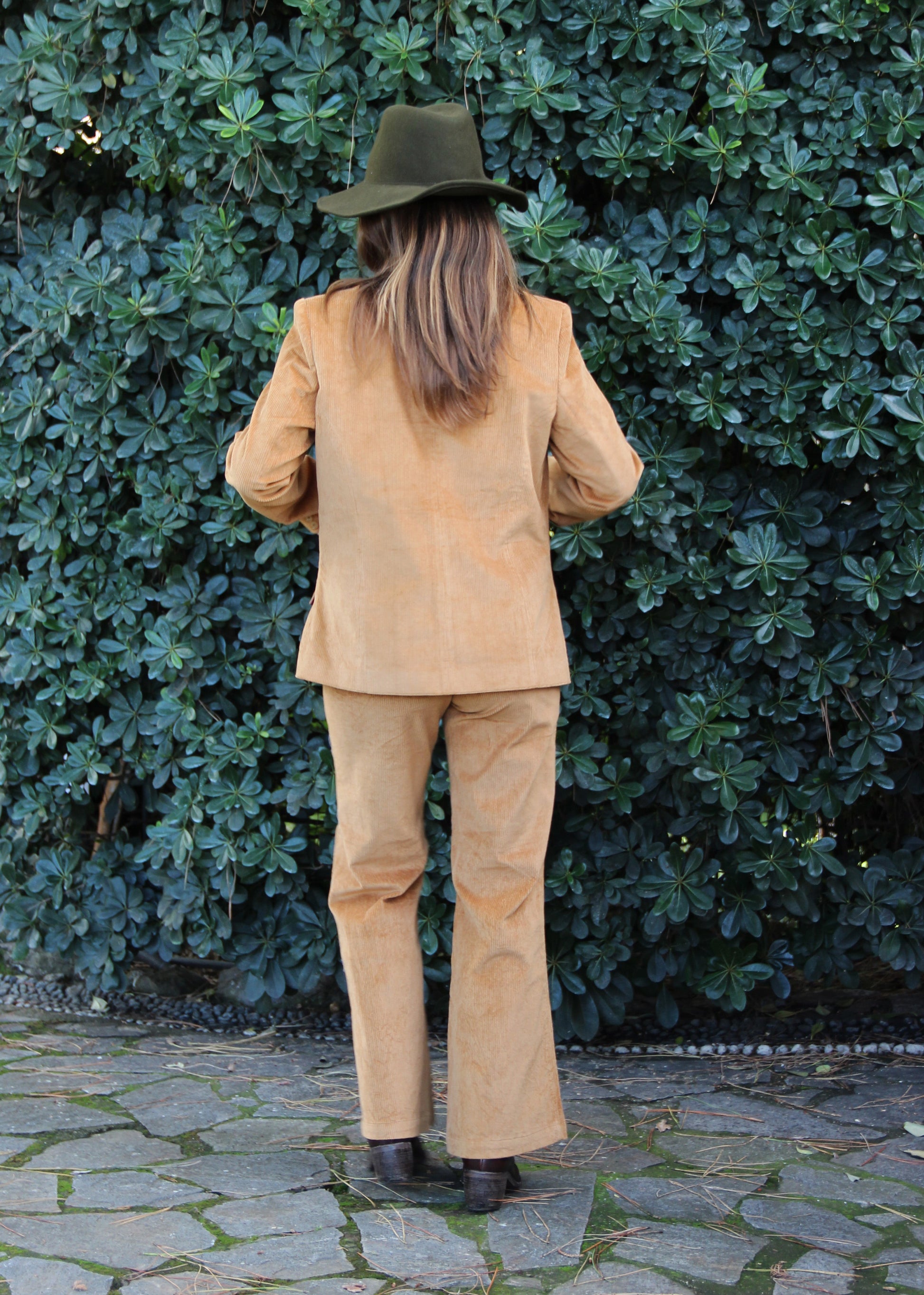 1970 Corduroy Suit in mustard, corduroy suit in mustard with jacket and pants. Jacket with fitted waist, structured shoulders, and mandarin collar. Polyester lining, model is 170 cm and is wearing size S. Pants in corduroy with front darts, regular fit, available in sizes M and L. Made in India with an elegant and versatile design. Dry clean only, iron on low heat, do not bleach.