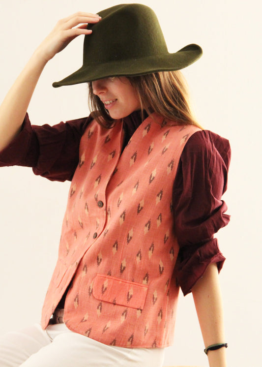 Gilet Madeleine in lino rosa di IGI Ama, smanicato rosa salmone con motivo a rombi, metà rosa chiaro e metà marrone. Realizzato in lino con pattern ikat e interno in velluto a coste. Stile elegante e raffinato, prodotto eticamente in India. Lavabile in lavatrice a 30°C, stirare a bassa temperatura.