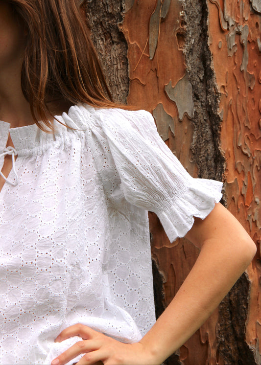 Blusa arricciata da donna in cotone bianco con trama sangallo, modello Pimpa shirt di IGI AMA, 100% cotone, con laccetto sullo scollo e maniche elasticizzate a sbuffo, tessuto elastico che si adatta a tutte le corporature, prodotta in India, ideale per look estivi e casual.