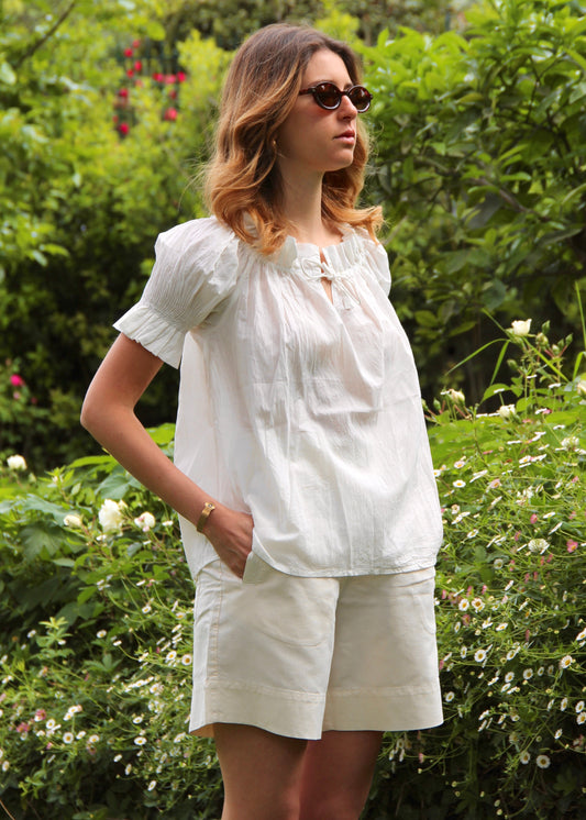Blusa arricciata da donna in cotone bianco, modello Pimpa shirt di IGI AMA, 100% cotone, con laccetto sullo scollo e maniche elasticizzate a sbuffo, tessuto elastico che si adatta a tutte le corporature, prodotta in India, ideale per look estivi e casual.