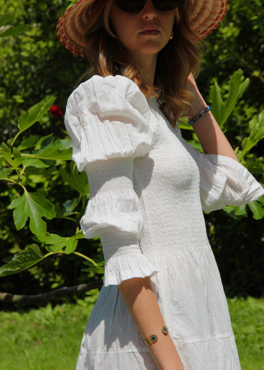 Primula Dress di IGI AMA, vestito midi in tessuto bianco 100% cotone, maniche lunghe a sbuffo con doppia cucitura elastica, busto arricciato, taglia unica e tessuto elasticizzato che si adatta a tutte le corporature, lunghezza fino alla caviglia, prodotto in India, ideale per un look comodo, femminile e artigianale.